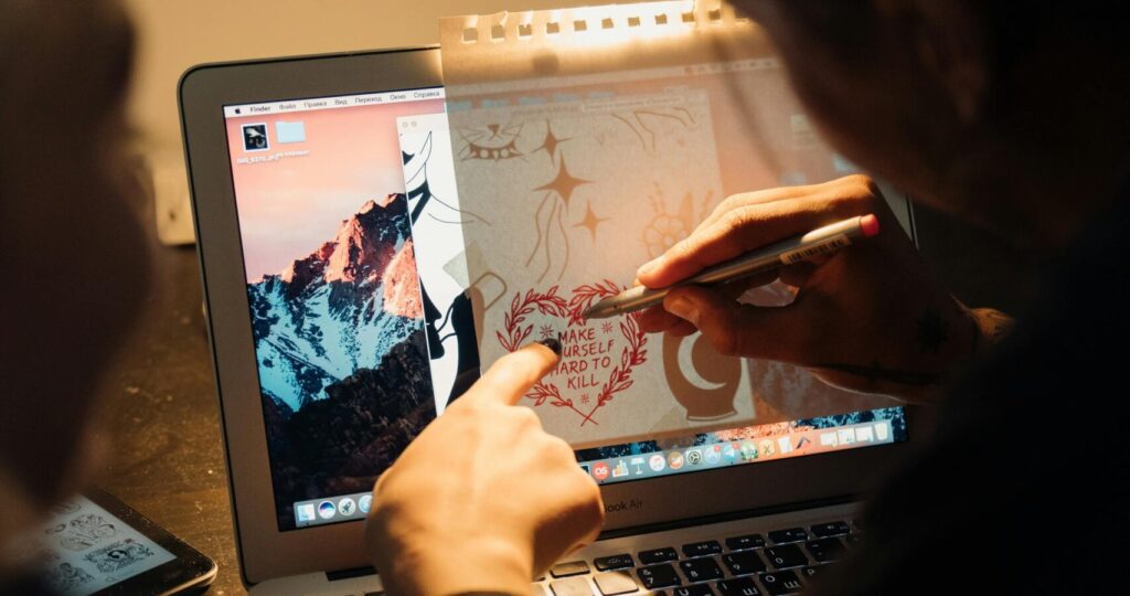 An artist sketches a design on a laptop, blending digital and traditional art techniques.