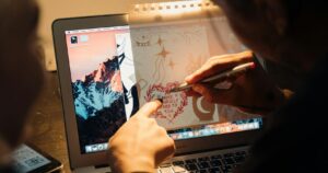 An artist sketches a design on a laptop, blending digital and traditional art techniques.